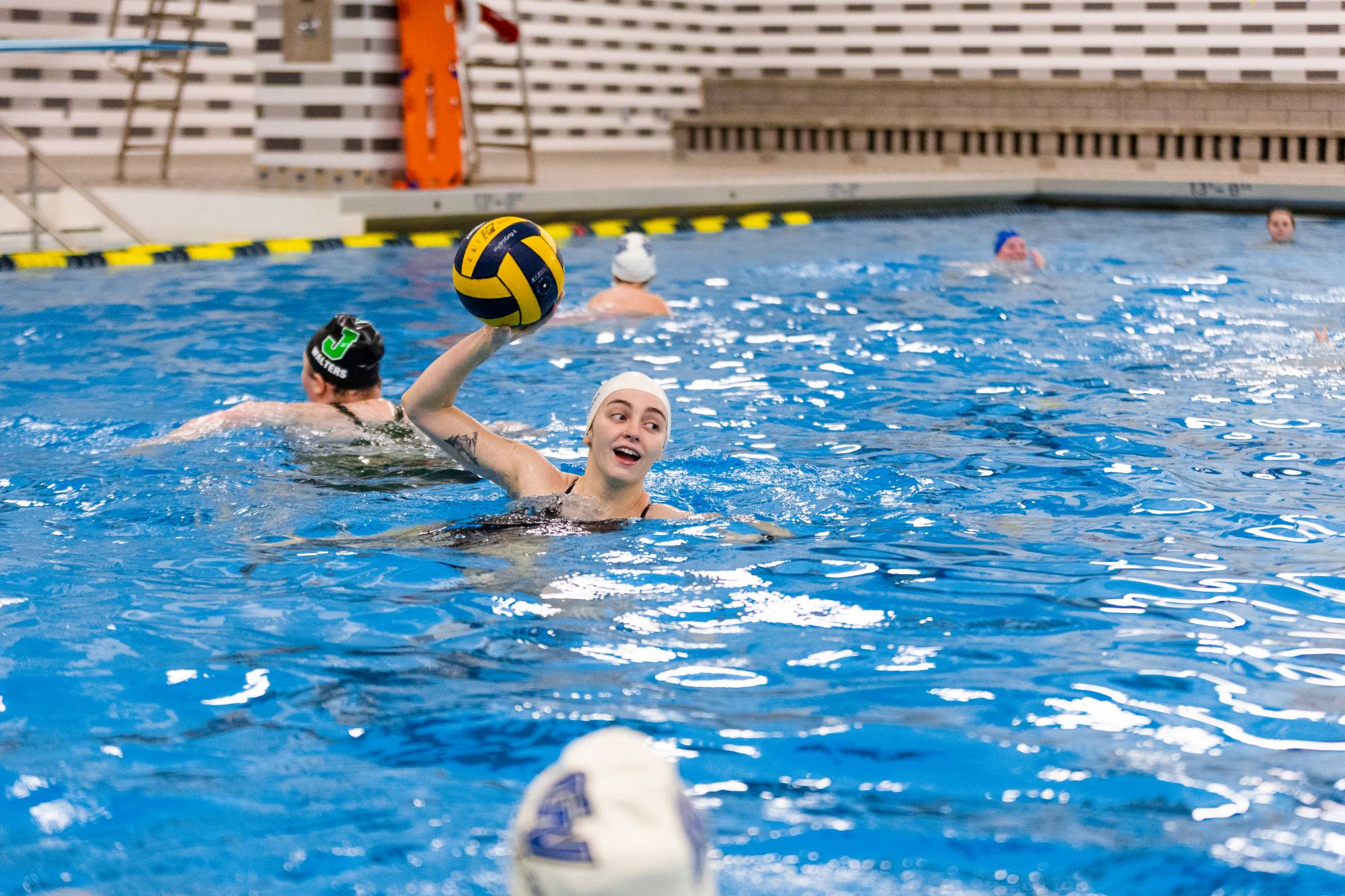 Student in a pool playing water polo. The student is holding the ball up in the air, preparing to throw.